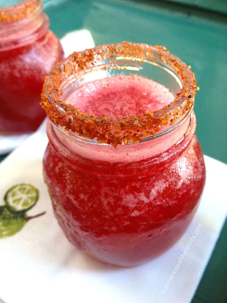 Red prickly pear margarita in a glass rimmed with Tajin, sitting on a napkin on a green drink tray