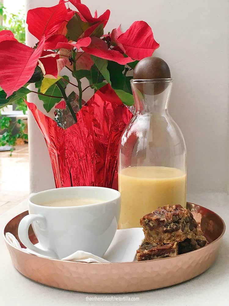 Rompope, also known as Mexican eggnog, served with holiday treats next to poinsettia flowers