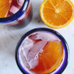 Spanish tinto de verano in two blue-rimmed glasses with orange slices floating on top. An orange on the side.