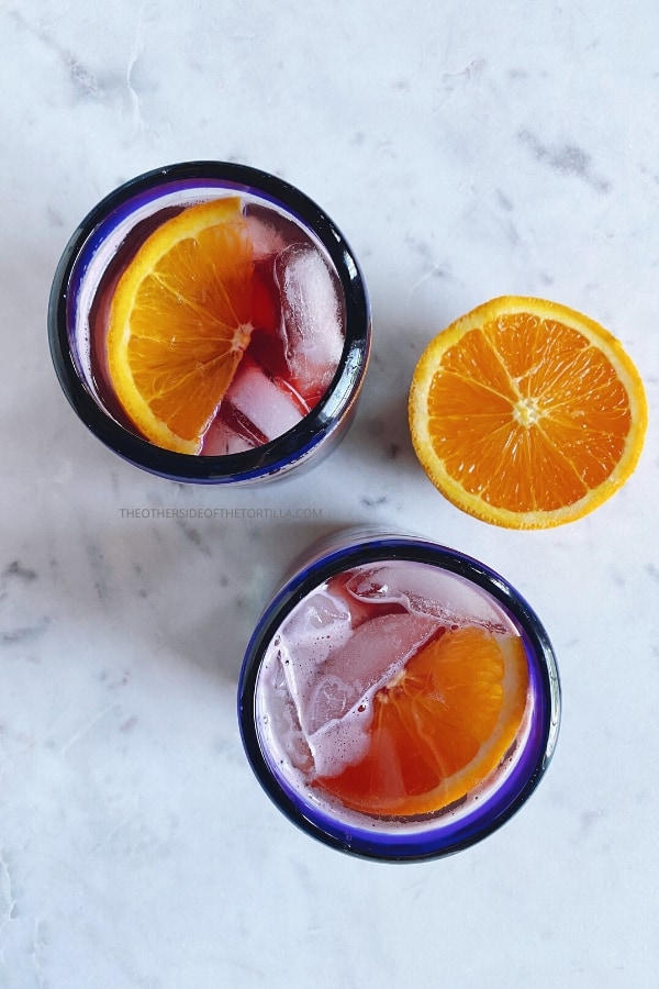 Two blue-rimmed glasses with tinto de verano, and ice cubes and orange slices floating on top