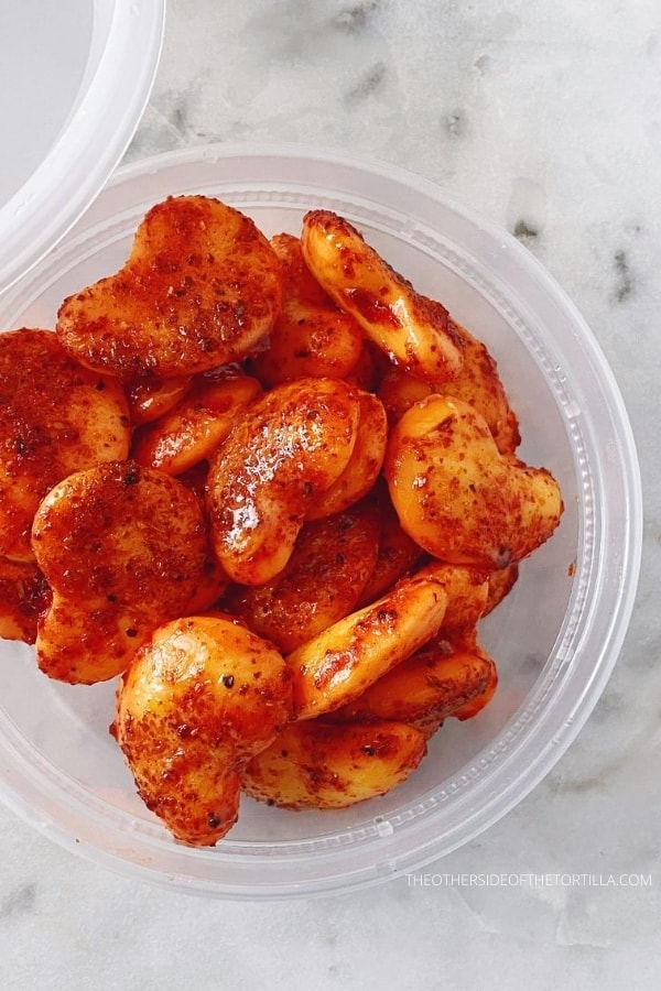 A round plastic container filled with spicy mango gummies dressed with Tajín and chamoy