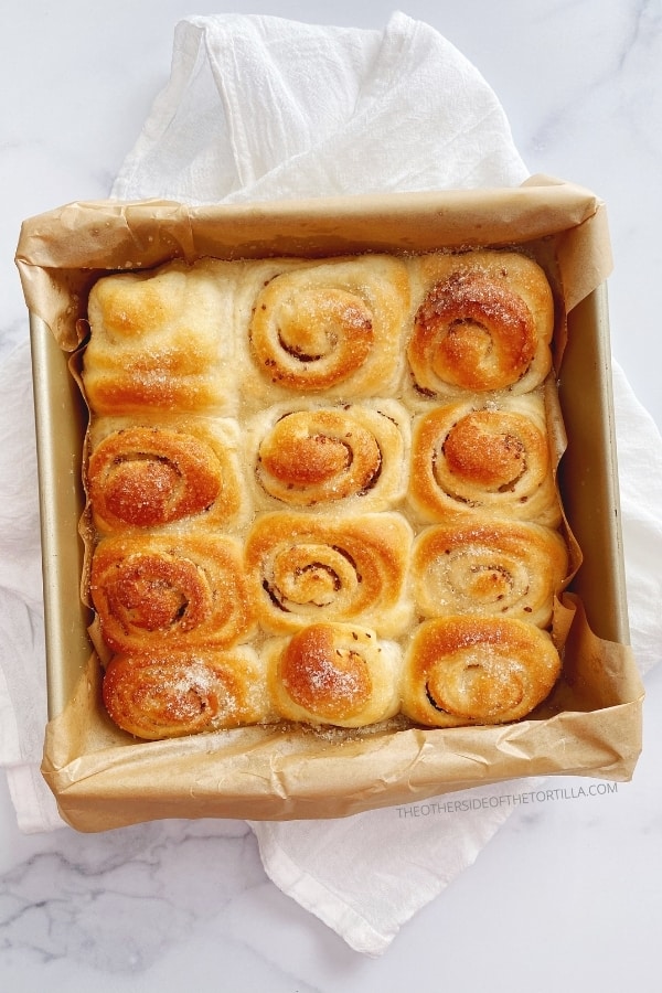 Anise rolls in a square baking pan over a white kitchen towel on a marble countertop