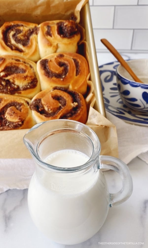 milk in a pitcher in the foreground in front of a pan of mexican cinnamon rolls fresh from the oven