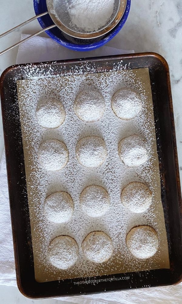 Mexican wedding cookies on a baking sheet with powdered sugar sifted over the tops