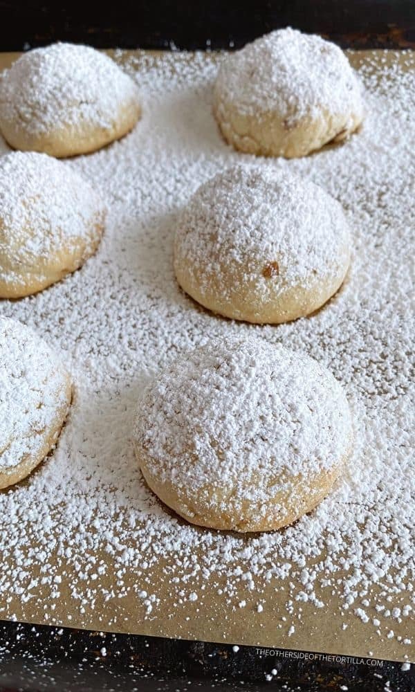 Mexican wedding cookies sprinkled with powdered sugar on a baking tray