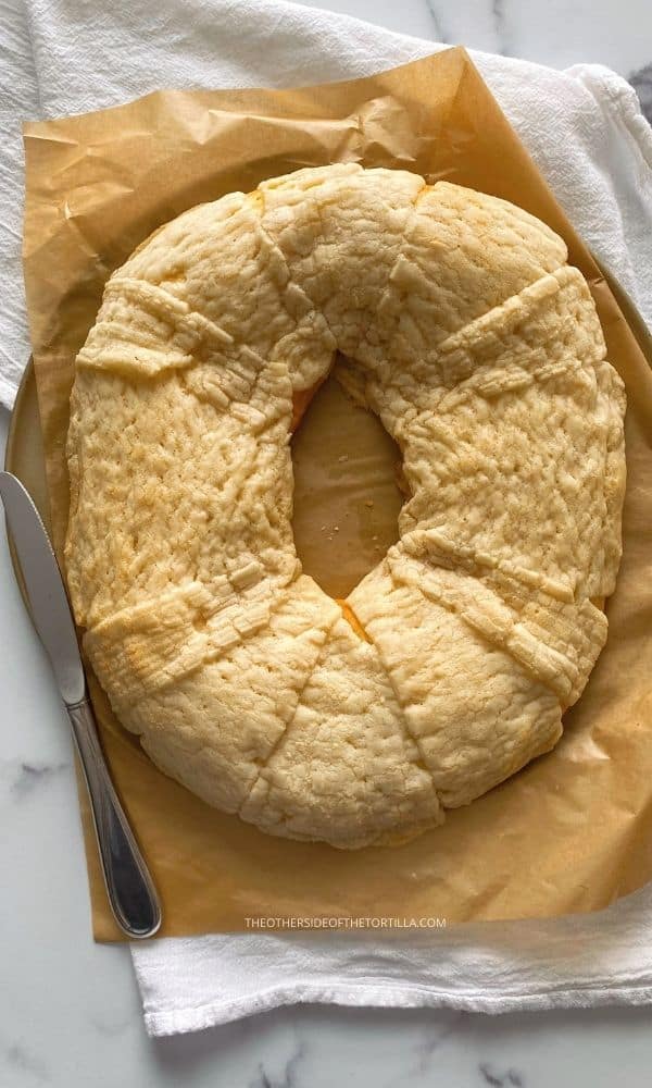 Sugar crunch topping Mexican rosca de reyes on top of brown parchment paper with a knife to the left of the cake